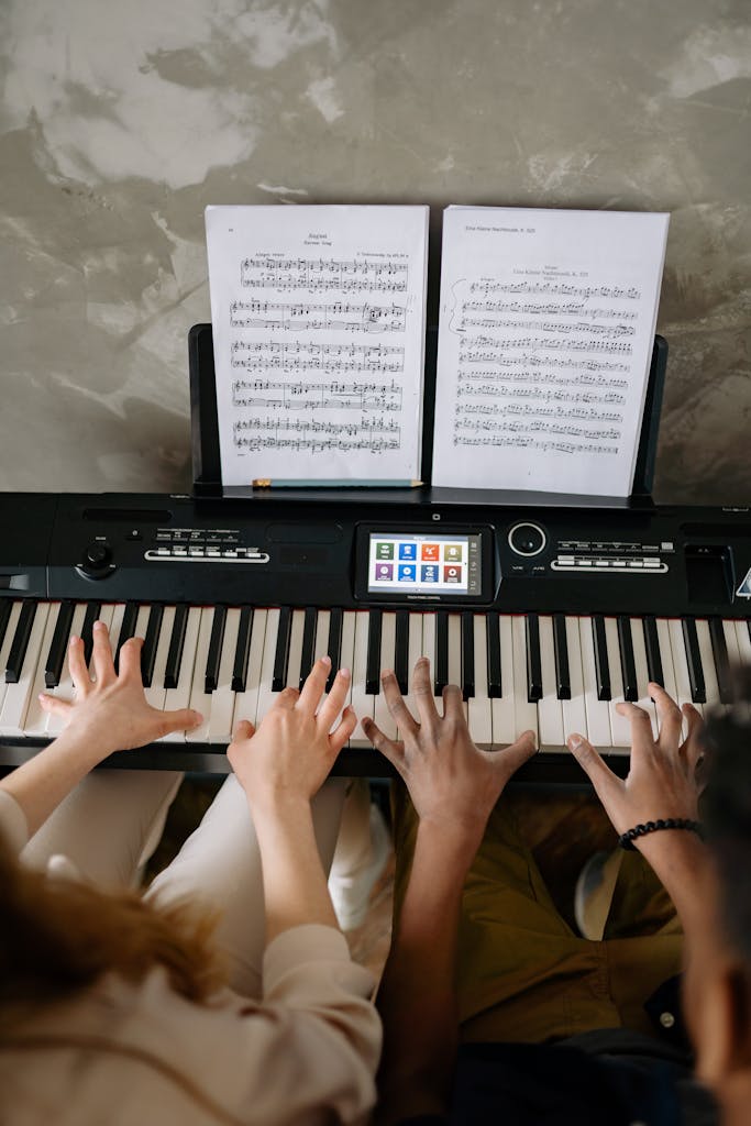 Top view of two people playing duets on a digital piano during music lessons.